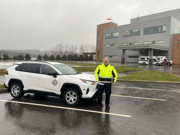 An MD3 physician in high-visibility gear beside the MD3 response vehicle outside a hospital